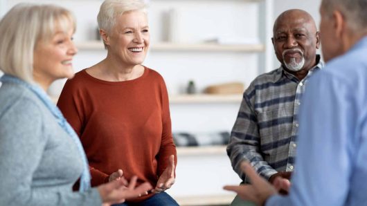 Excited multiethnic elderly people attending group therapy session at nursing house, positive senior man and woman sitting in circle, having conversation with psychologist and gesturing, closeup