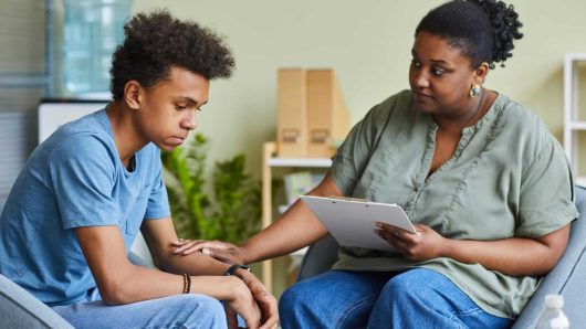 African psychologist supporting depressed teenage boy feeling guilty about behavior during therapy at office