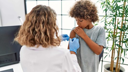 Mother and son wearing doctor uniform putting band aid on child arm at clinic